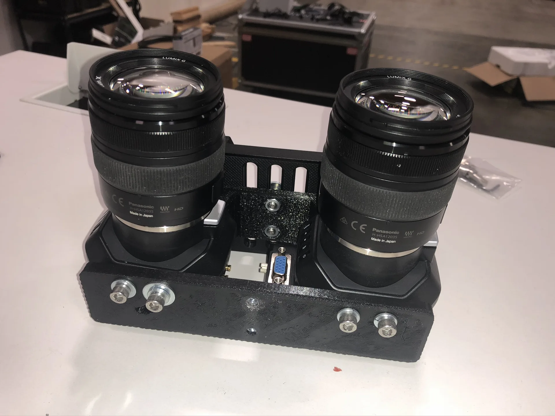 The two cameras side by side in the black cage on a white desk in a workshop.